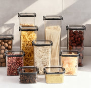 Set of clear food storage containers with black lids, each filled with different types of food on a white surface.