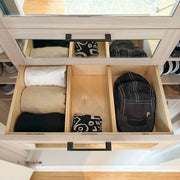 Open drawer with folded clothes and a cap inside, with a mirror reflecting part of the room.