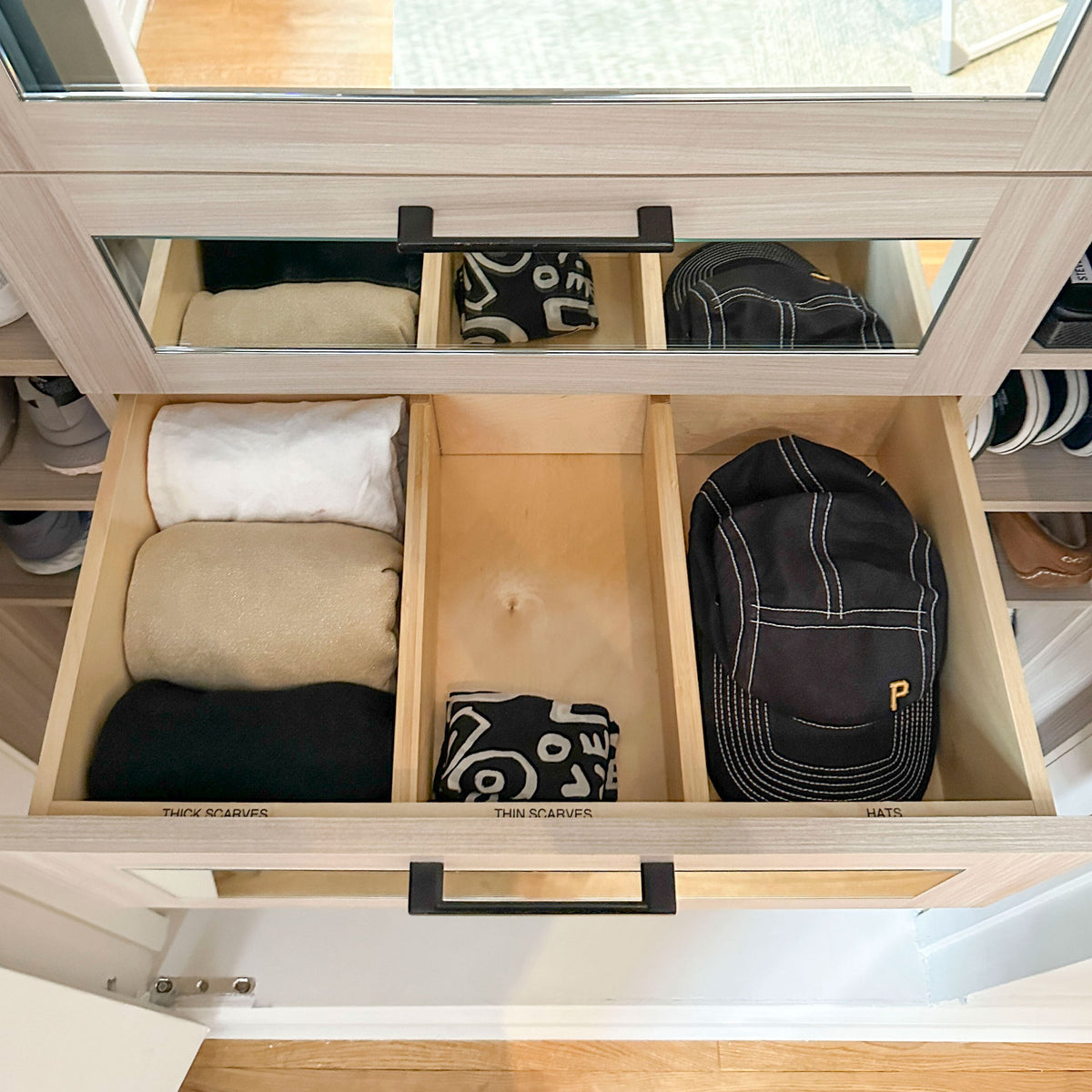 Open drawer with folded clothes and a cap inside, with a mirror reflecting part of the room.