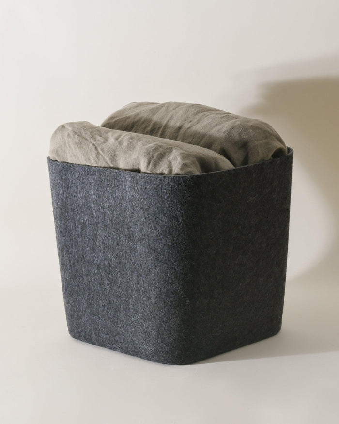 Dark gray ottoman with a cushion on a light background