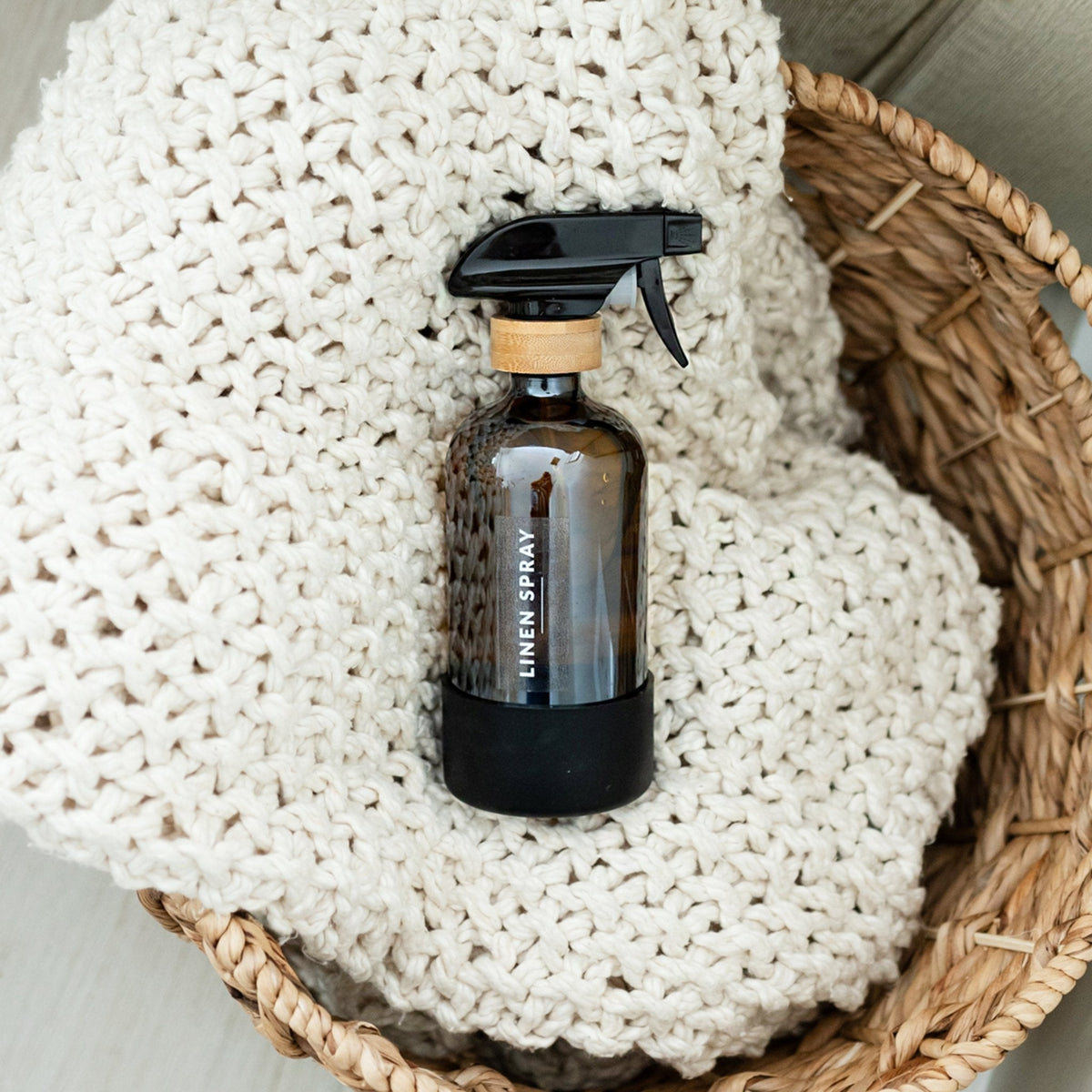 Brown spray bottle labeled 'Linen Spray' on a textured white fabric inside a woven basket.