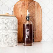 Bottle of red wine vinegar on a kitchen counter with a wooden cutting board and decorative jar.