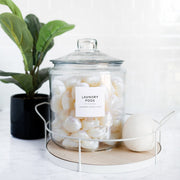 Clear glass jar with laundry pods on a white surface with a plant in the background